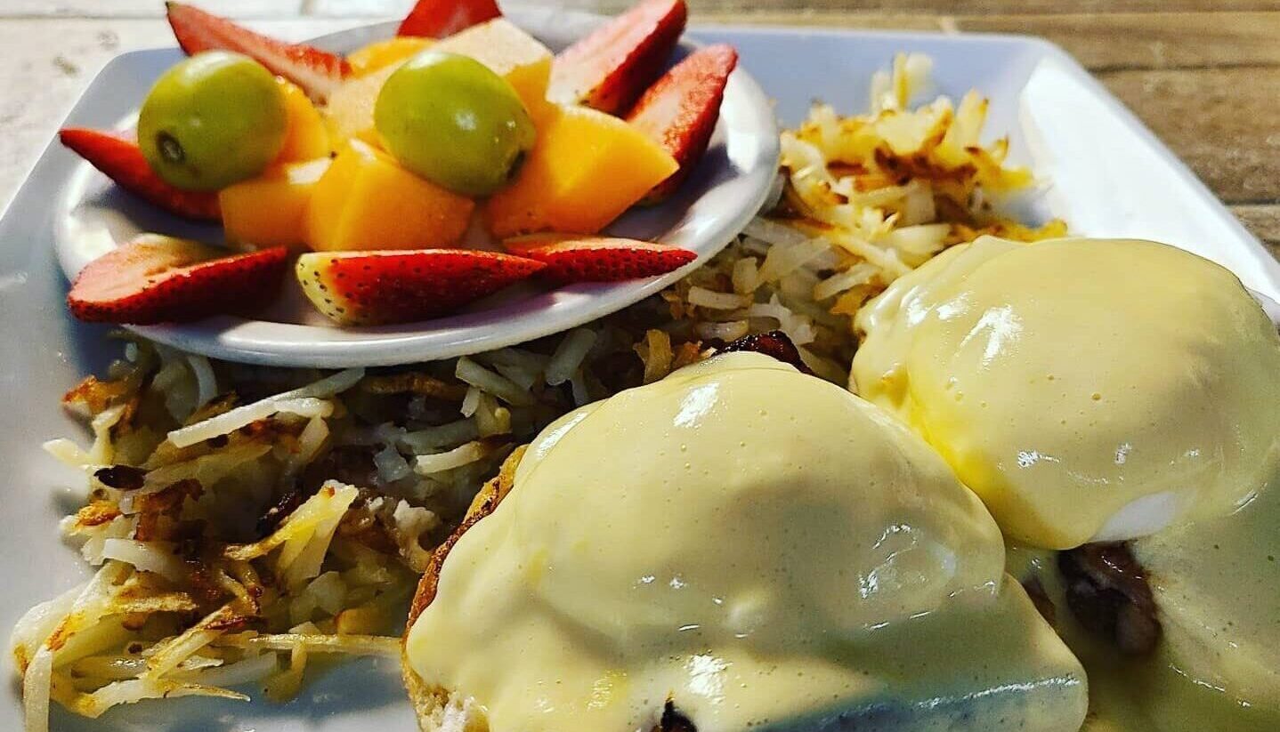 eggs benedict and hashbrowns plate with fruit on the side